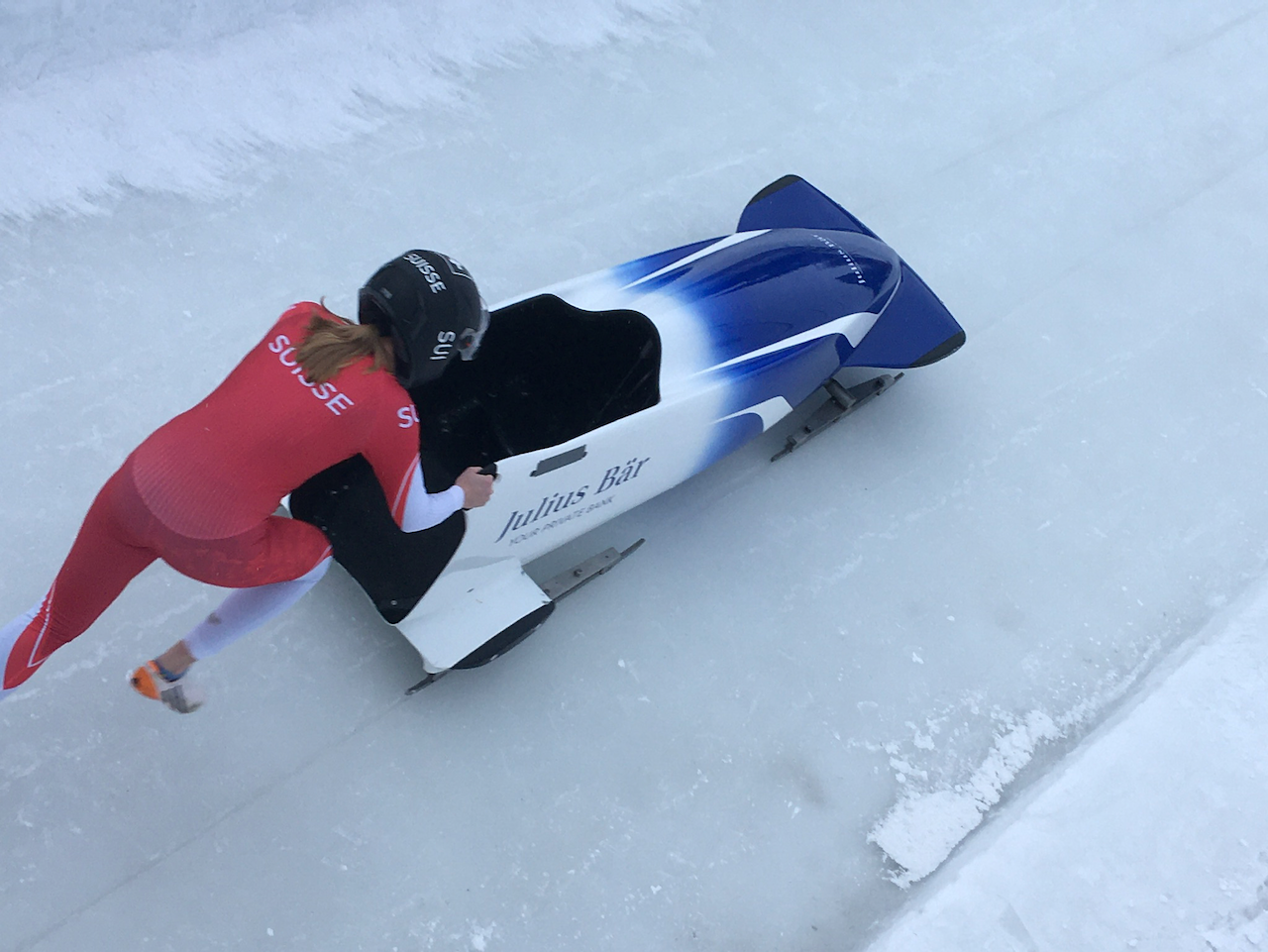 A blue and white monobob is being pushed by an athlete in.a red suit.